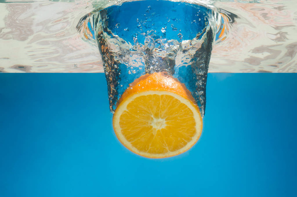 Orange splashing in water with blue background - Photo, Image