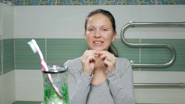 Fiatal, vonzó nő használ fogselymet, a fürdőszobában a hotelszobában. Ő gondosan chitit lyukak a fogak között, ellenőrizze a végén az eredmény - Felvétel, videó