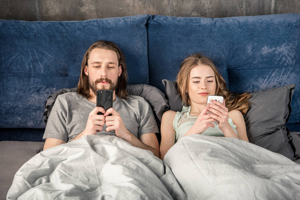 Casal na cama com smartphones
 - Foto, Imagem