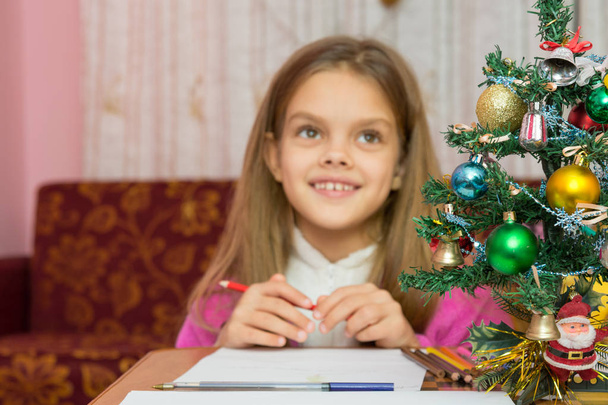 Happy little girl thinking of a gift for the new year, focusing on a fur-tree - Foto, Imagem
