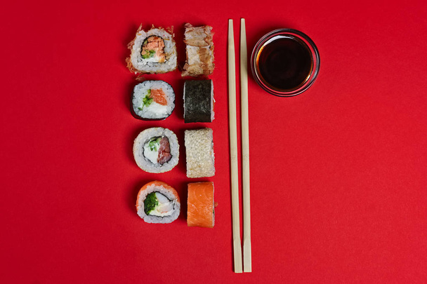 Set of salmon rolls, soy sauce and chopsticks on red background - Foto, Imagen
