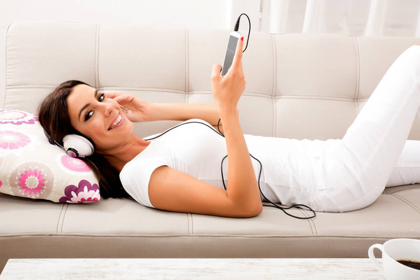 Beautiful young woman laying on the couch, listening to music  - Photo, Image