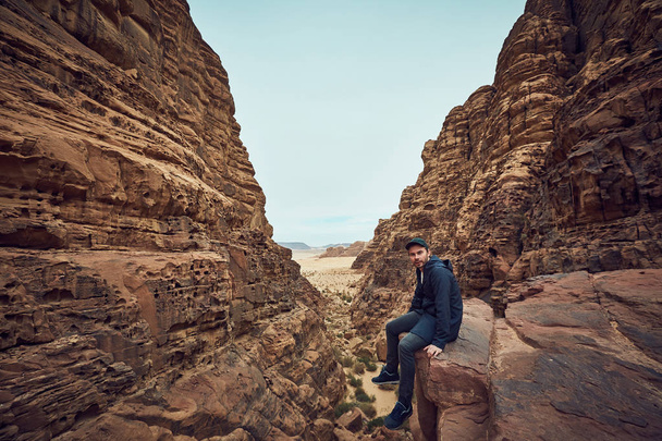 Middle-age man in dark clothes sitting on red rock in Wadi Rum desert in Jordan - Foto, afbeelding