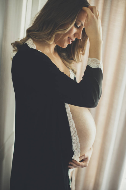 Fiatal terhes nő az ablak - Fotó, kép