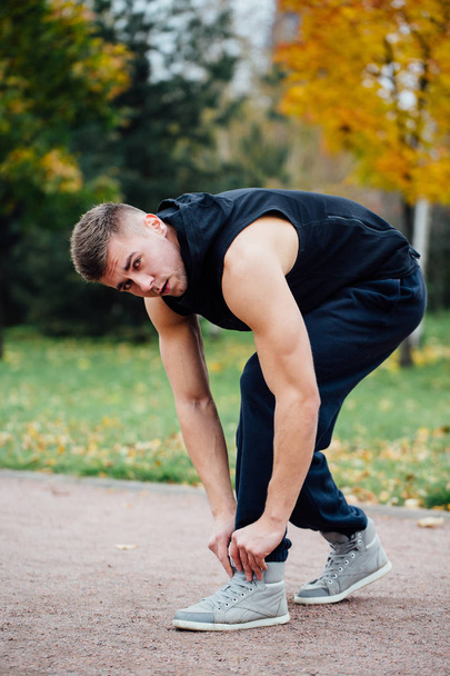 Fitness mies sitoa kengännauhat syksyllä puistossa
. - Valokuva, kuva