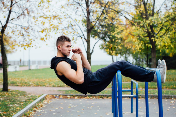 Fitness man doing stomach workouts on horizontal bar outdoors - Photo, Image