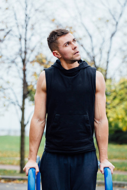 portrait of  focused muscular young man in black workout clothes doing dips on parallel bars. - Foto, Bild
