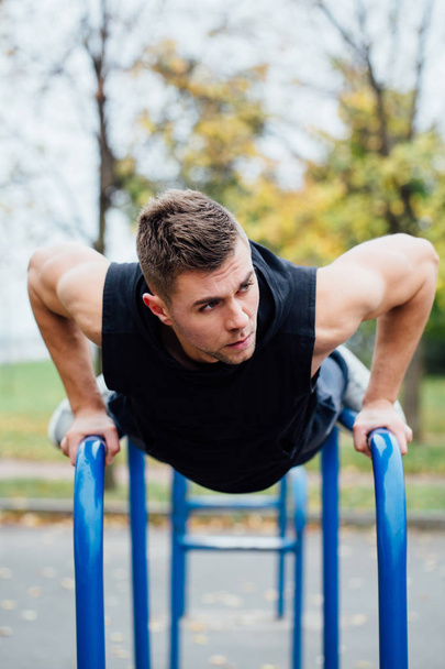 portrait of  focused muscular young man in black workout clothes doing dips on parallel bars. - Fotó, kép