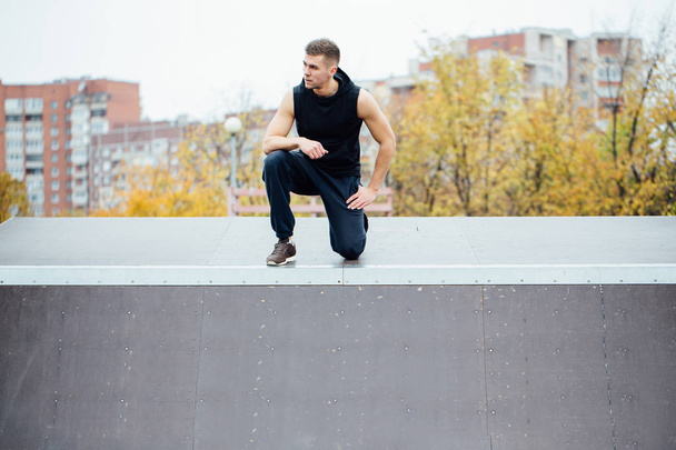 Portrait of a confident fitness guy. Man poses on skate ramp, against the background the city. - Photo, Image