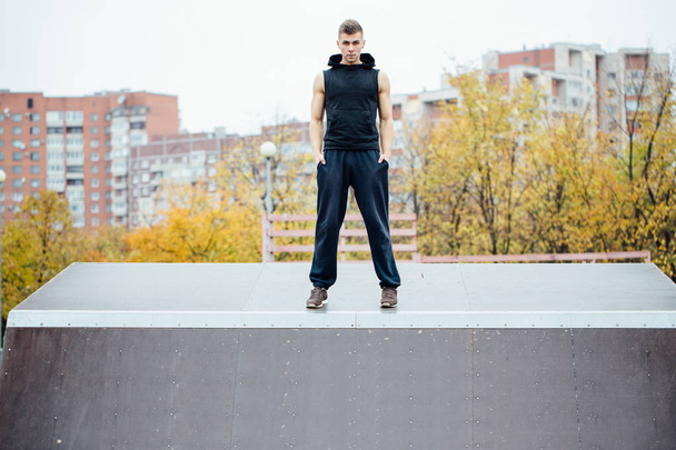 Portrait of a confident fitness guy. Man poses on skate ramp, against the background the city. - Foto, immagini