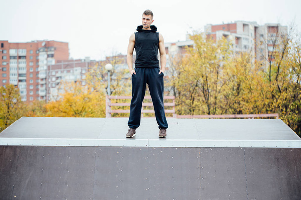 Portrait of a confident fitness guy. Man poses on skate ramp, against the background the city. - Fotografie, Obrázek