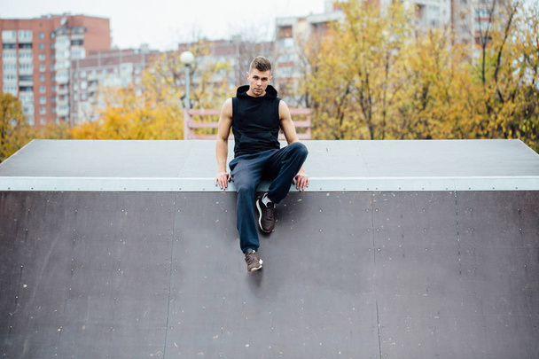 Portrait of a confident fitness guy. Man poses on skate ramp, against the background the city. - Foto, Imagen