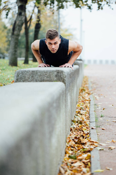 Male runner doing exercise, workout in the fall park. Push ups with bench. - Foto, Imagem