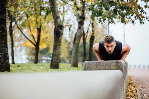 Male runner doing exercise, workout in the fall park. Push ups with bench. - Фото, зображення