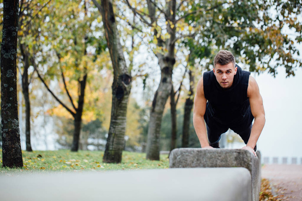 Corredor masculino haciendo ejercicio, entrenamiento en el parque de otoño. Push ups con banco
. - Foto, Imagen