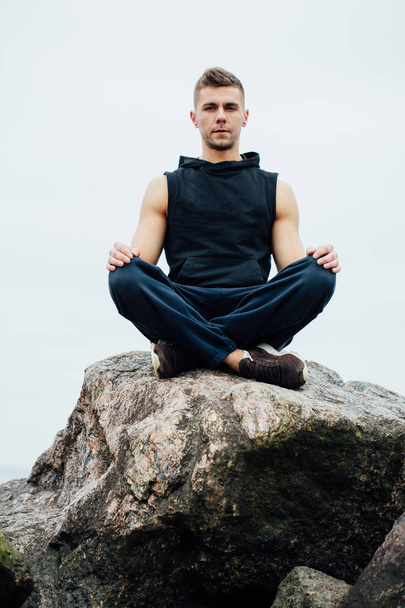 Strong fitness yoga man in lotus pose on the rock beach near the ocean. Harmonic concept. - Foto, afbeelding
