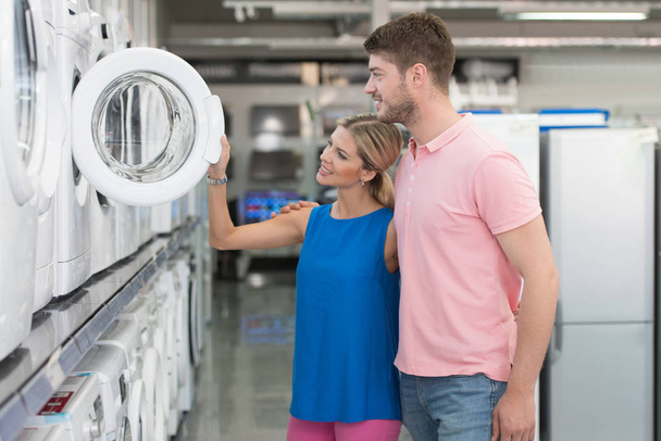 Smiling Couple Buying Washing Machine In Supermarket - 写真・画像