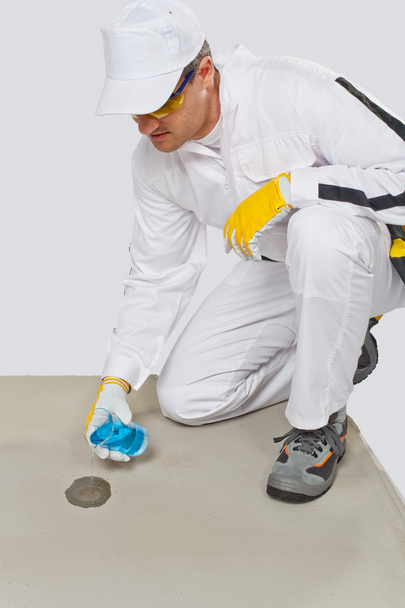 Trabajador con frasco de vidrio de agua probando la humedad del cemento
 - Foto, Imagen