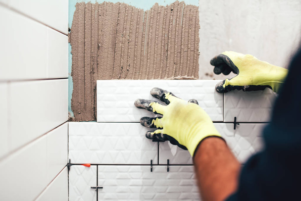 industrial construction worker installing small ceramic tiles on bathroom walls and applying mortar with trowel - Fotó, kép