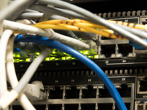 Rows of multiple fiber and ethernet cables plugged into a router (switch), with green activity lights. The network installed in the rack. Data center, wired network, switch panel, rack. - Photo, Image