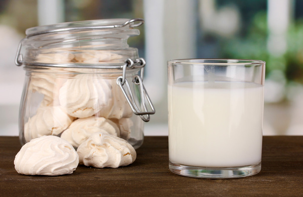 Glass of milk with meringues on wooden table on windows background close-up - Foto, Imagen