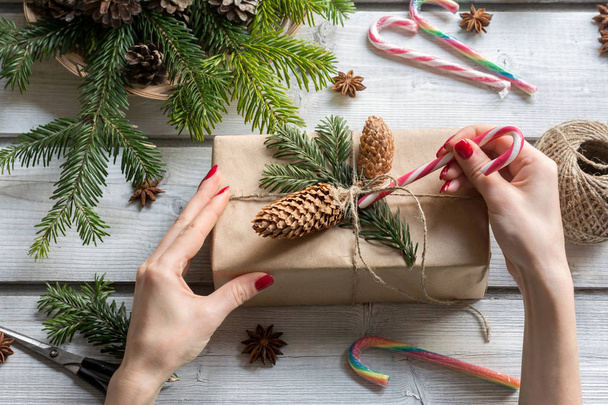 Woman decorating Christmas present with candy cane, cones and spruce branch - Foto, afbeelding