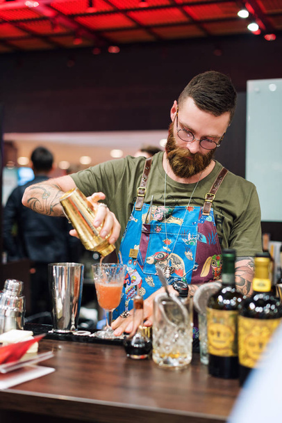 Kyiv, Ukraine - 30 october, 2016: Barman festival. Handsome bearded hipster with long beard and mustache holding shaker, making alcoholic cocktail. - Photo, Image