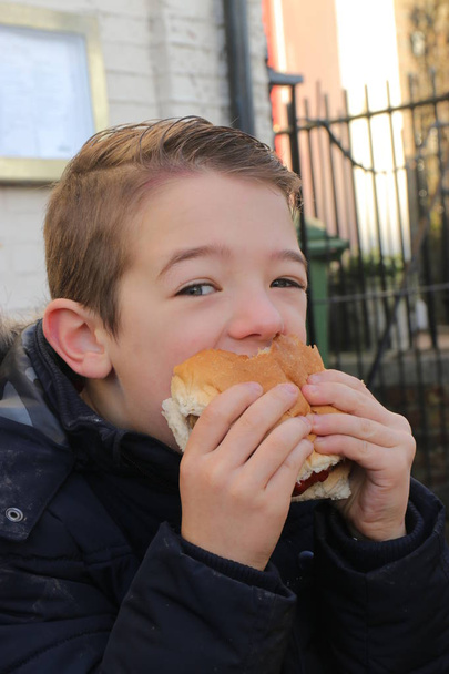 A handsome young boy eating a beef burger - Photo, Image
