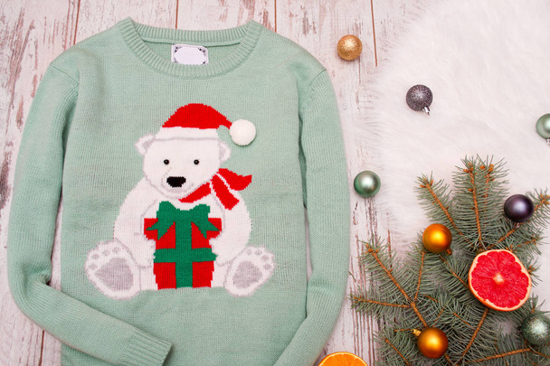 Зелений светр з ведмедем на дерев'яному тлі. Гілка ялинки з різдвяними прикрасами. Вид зверху
 - Фото, зображення