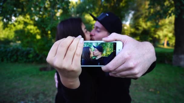 愛するカップルが作る Selfie、ハグやオープンエアのグリーンパークでカメラのポーズの手と電話を保持します。. - 映像、動画