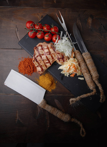 Pork steak grilled with various vegetables and spices on a dark background. - Φωτογραφία, εικόνα
