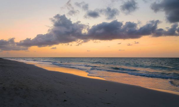 a beautiful calm sunset at the Atlantic Ocean, on the coast of Varadero, Cuba, with all the spectr of colors, red, orange, and yellow dominating, light breeze, sun hiding behind the horizon line, sky dark and full of cotton clouds - Photo, Image