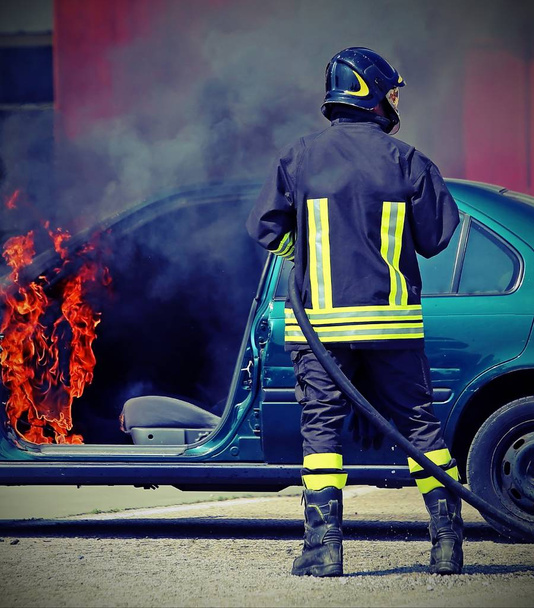 brandweerman tijdens het afsluiten van een brand van een auto - Foto, afbeelding