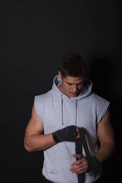 Athletic man bandaging his hands for boxing bandages. A man dressed in a gray hoodie. - Foto, Imagen