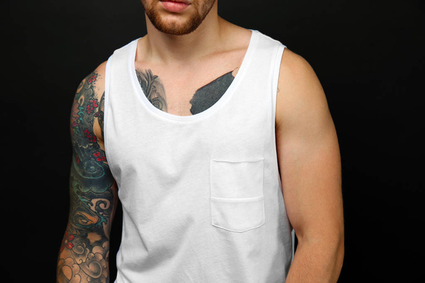 Young tattooed man posing on dark background - 写真・画像