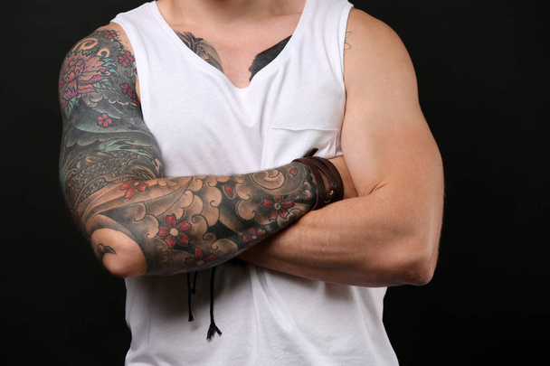 Nuori tatuoitu mies poseeraa tummalla taustalla
 - Valokuva, kuva