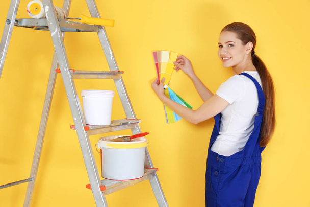 Beautiful young decorator selecting color of wall, on yellow background - Фото, изображение