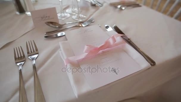 Decoración de mesa festiva arreglada de cerca - menú y servilleta atada con cinta rosa. Conjunto de vajilla para ocasión especial de banquete de bodas, recepción de aniversario o almuerzo de cumpleaños en un restaurante de lujo
 - Imágenes, Vídeo