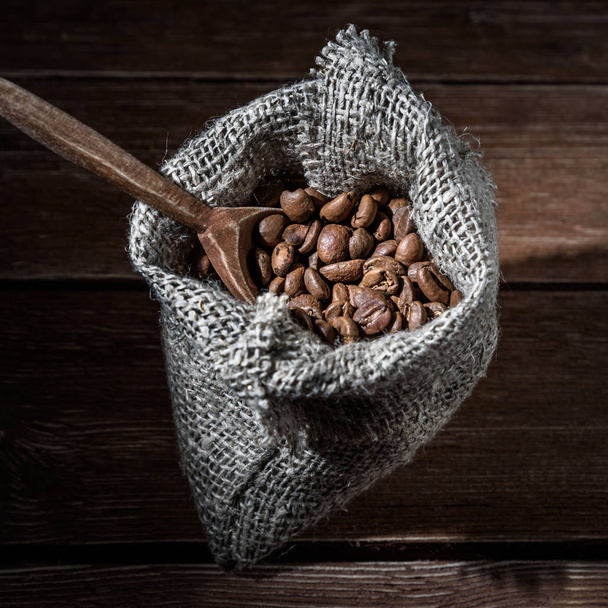 Coffee beans in a hessian sack and scoop on brown wooden background - Zdjęcie, obraz