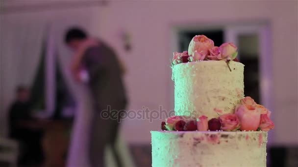 Hombre y mujer bailando en el fondo de la hermosa tarta de boda decorada con rosas naturales florece y bayas de cerca. Recepción de banquetes y catering. Decoración floral en cocina
 - Imágenes, Vídeo