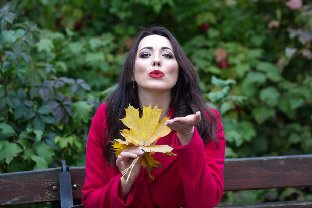 Красивая задумчивая женщина в красном пальто с желтыми листьями
 - Фото, изображение