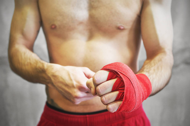 Человек заворачивает руки в красные боксёрские обертки
.  - Фото, изображение