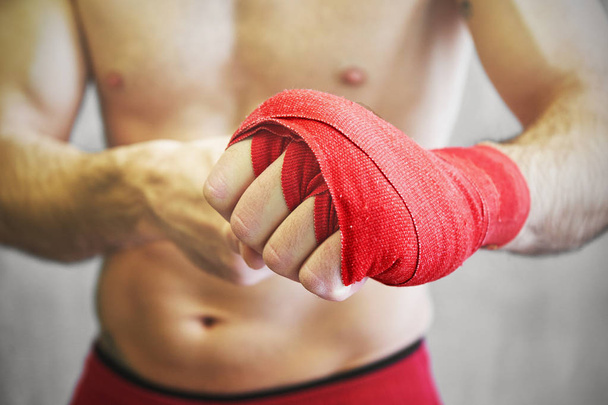 El hombre está envolviendo las manos con envolturas rojas de boxeo
.  - Foto, Imagen