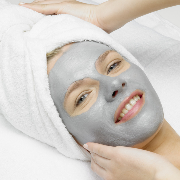 toepassing van een cosmetische masker op het gezicht van jonge vrouw op de schoonheidsspecialiste - Foto, afbeelding