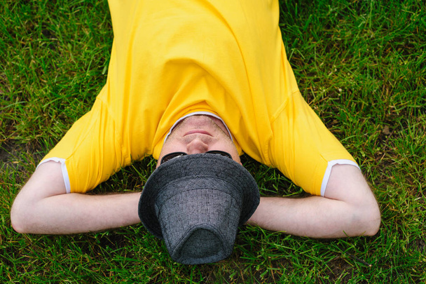 ember a sárga pólót és kalap feküdt a fűben - Fotó, kép