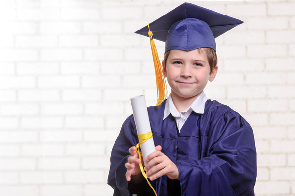 Menino da escola primária em copo e vestido posando com diploma
 - Foto, Imagem
