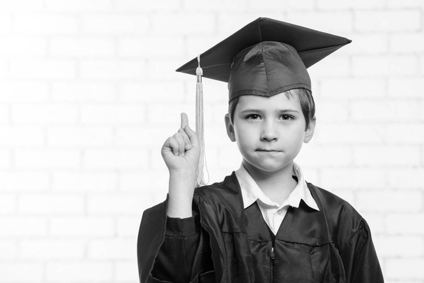 Primary school boy in cup and gown posing with his finger - Foto, afbeelding