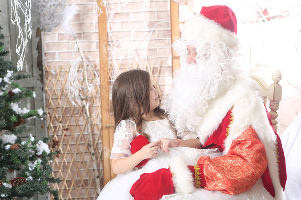 Santa Claus con una gorra roja sosteniendo a un bebé de rodillas
 - Foto, imagen