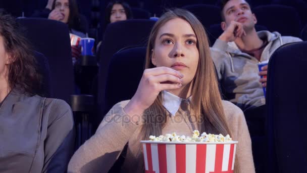 Girl slowly puts the popcorn in her mouth at the movie theater - Footage, Video