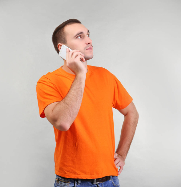 Handsome man talking by mobile phone on light background - Foto, afbeelding